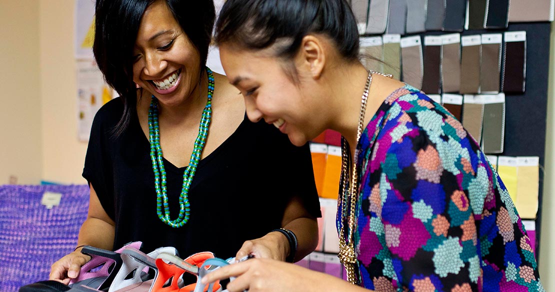 Two women smiling and working together while reviewing at shoe materials.