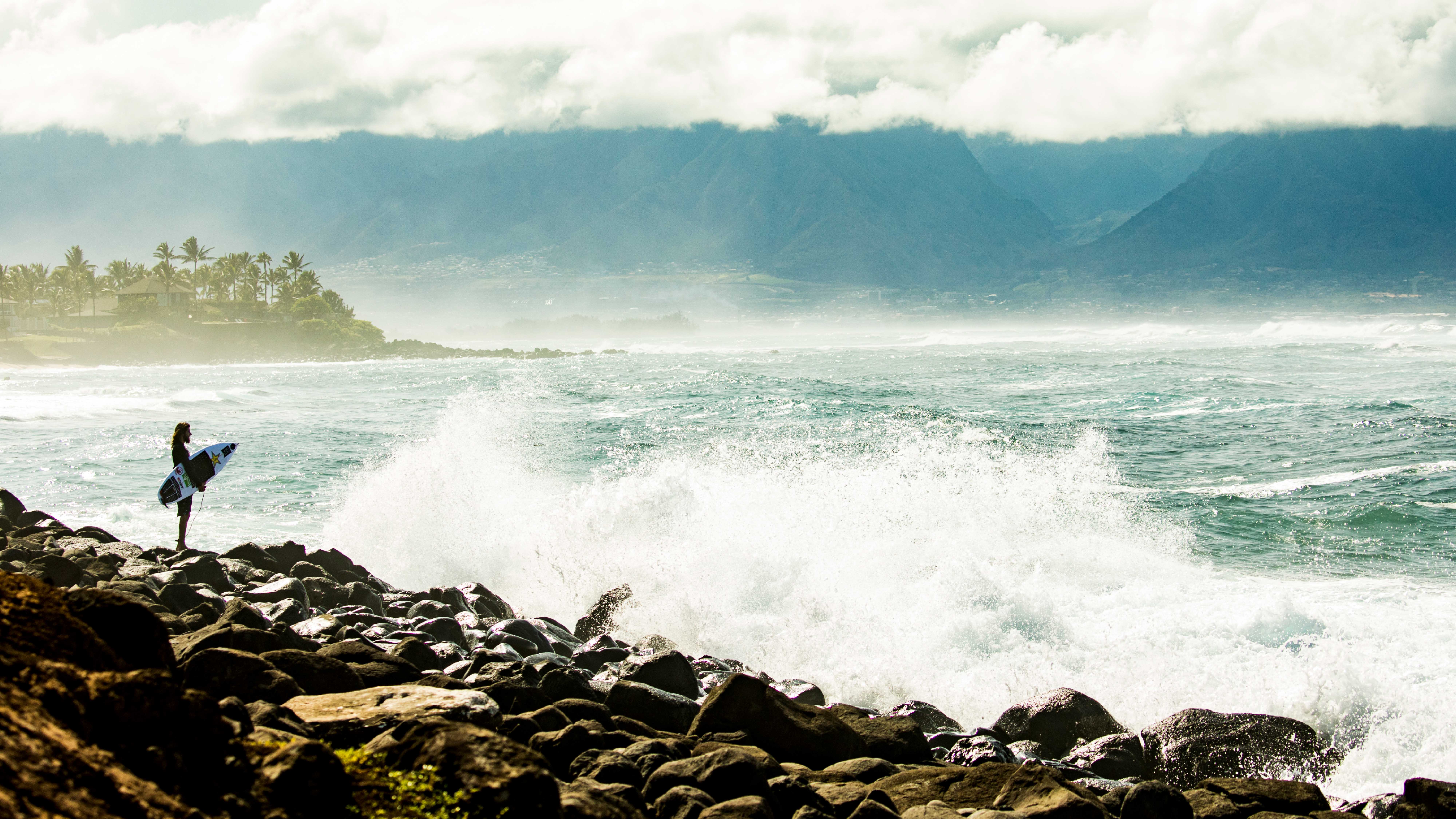 surfer standing on rock point overlooking ocean waves
