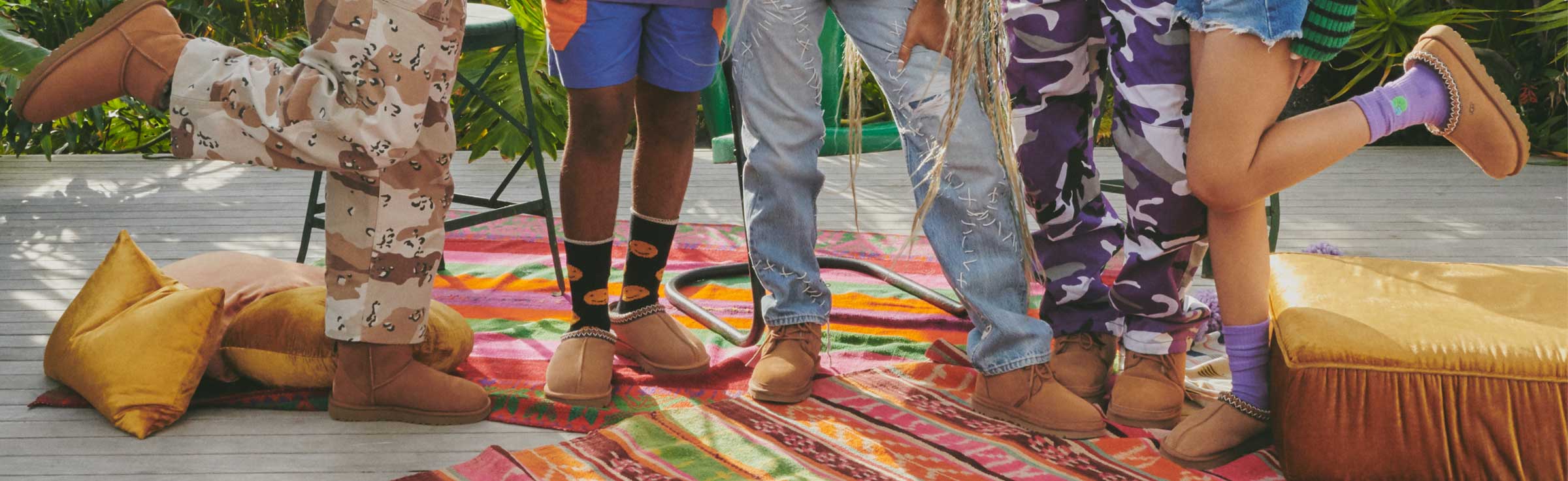Five pairs of legs with UGG chestnut slippers and boots on colorful rugs